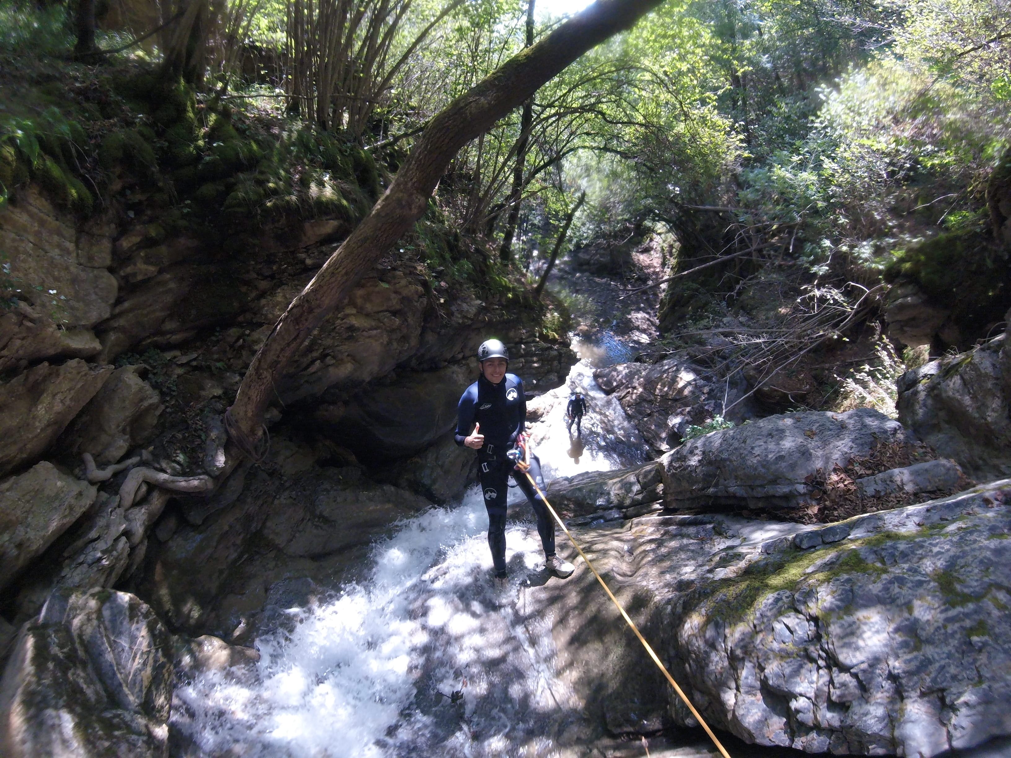 Participant de barranquisme baixant en ràpel per una cascada rocosa al bosc dens del Barranc del Pamano