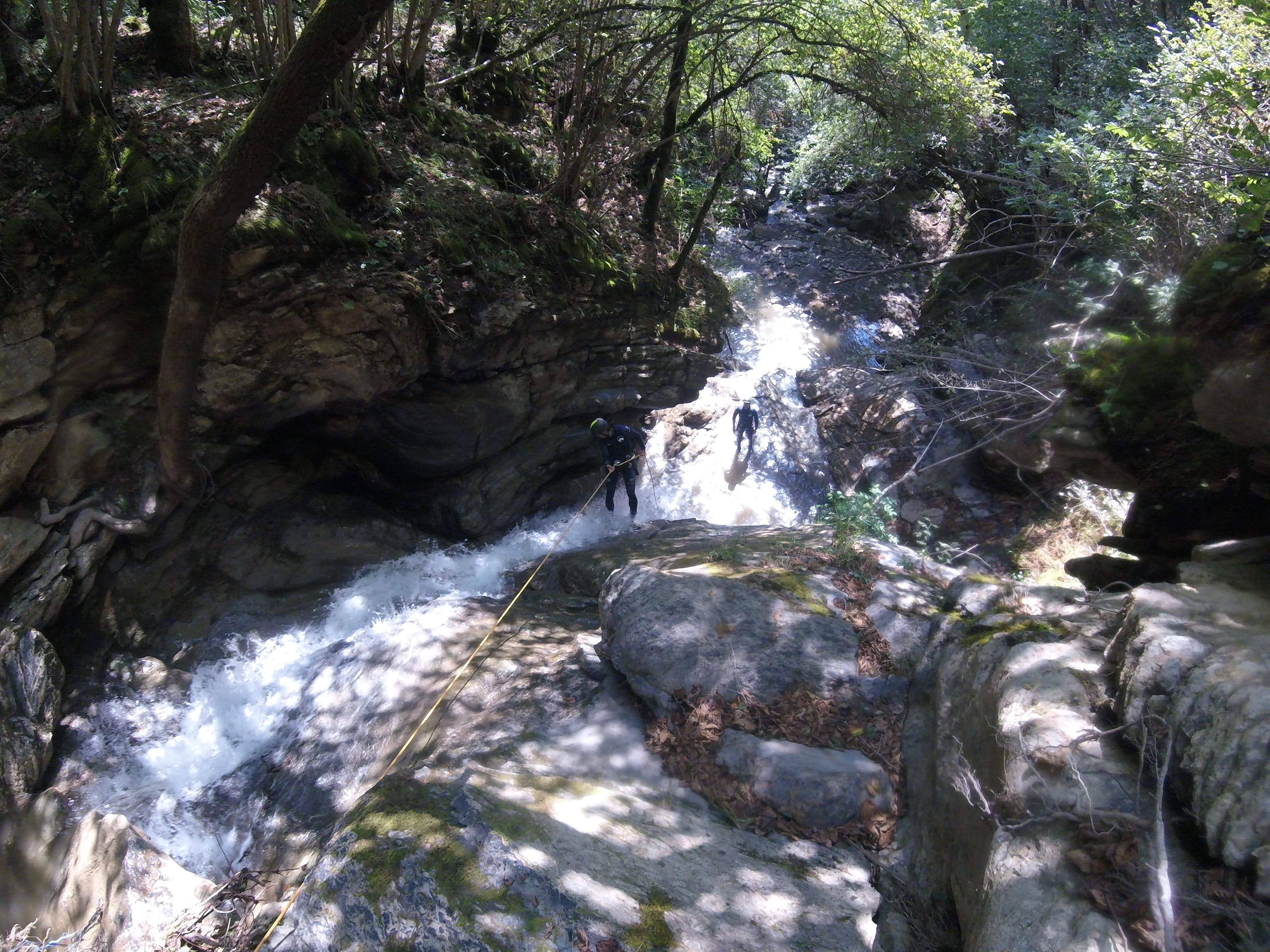 Participants de barranquisme baixant per una cascada rocosa amb corda al bosc dens del Barranc del Pamano