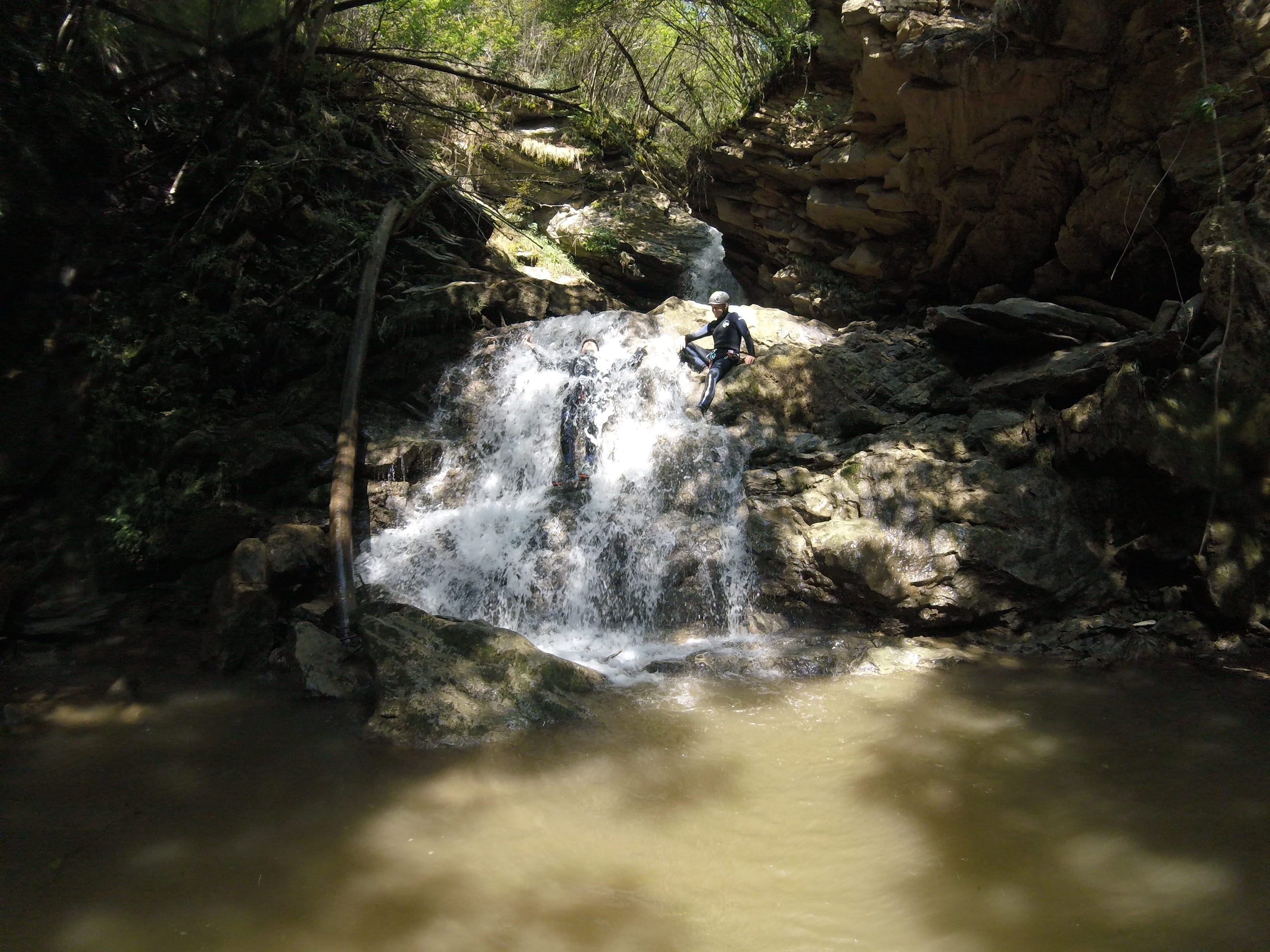 Participant de barranquisme baixant per una petita cascada fins a una poza al bosc del Barranc del Pamano