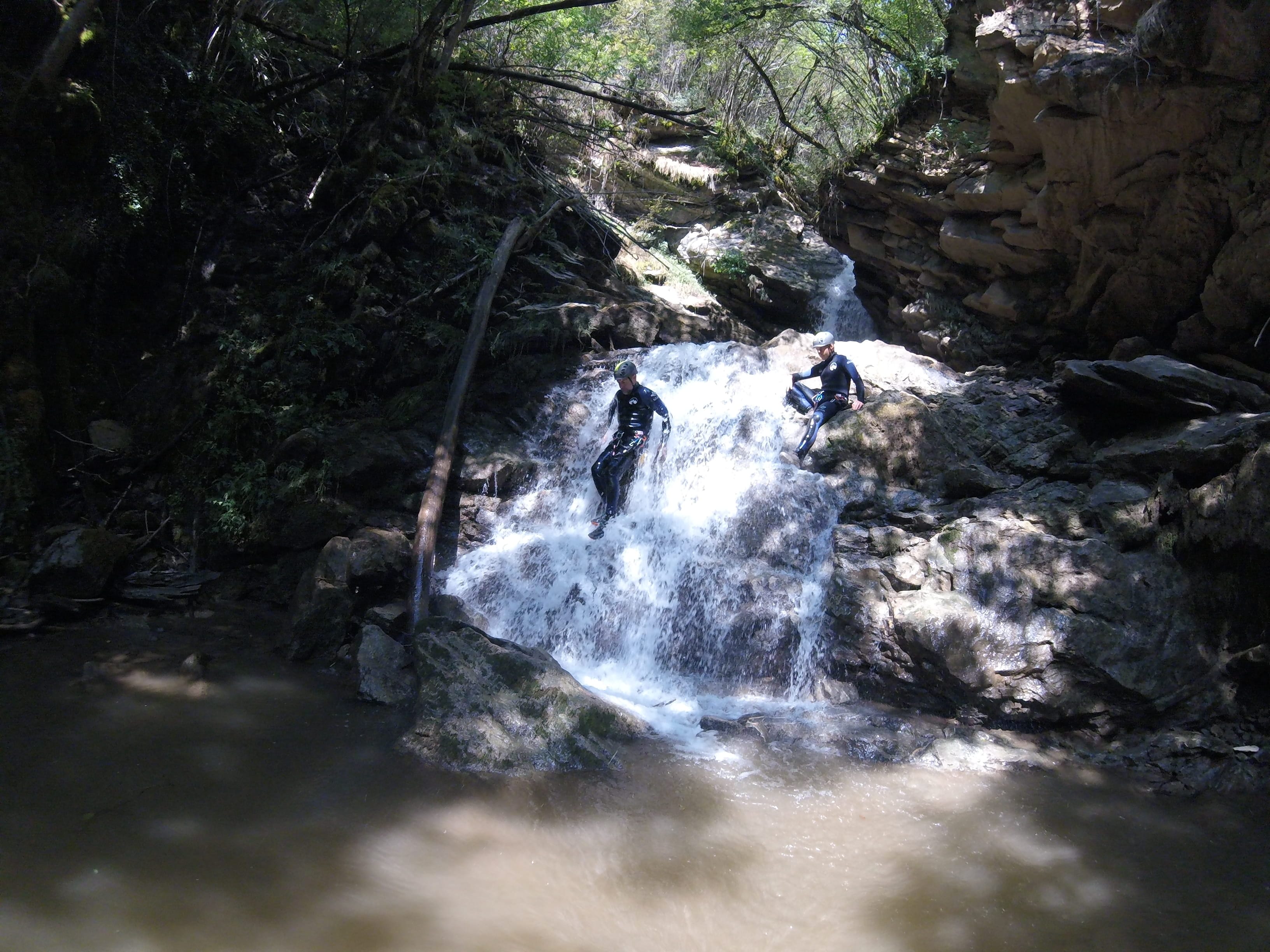 Dos participants de barranquisme baixant per una petita cascada envoltada de bosc dens al Barranc del Pamano