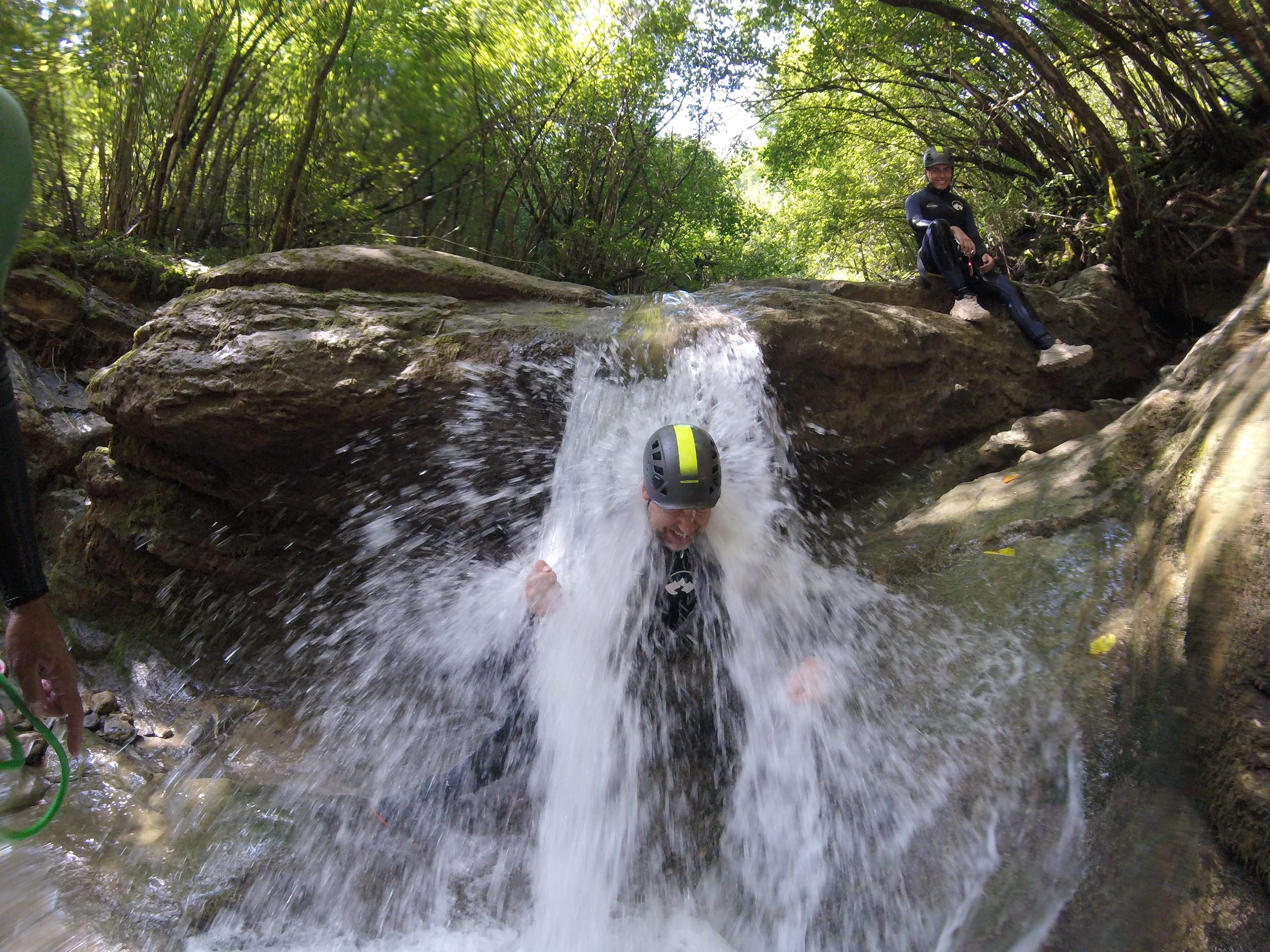 Participant de barranquisme passant directament sota una petita cascada al bosc del Barranc del Pamano