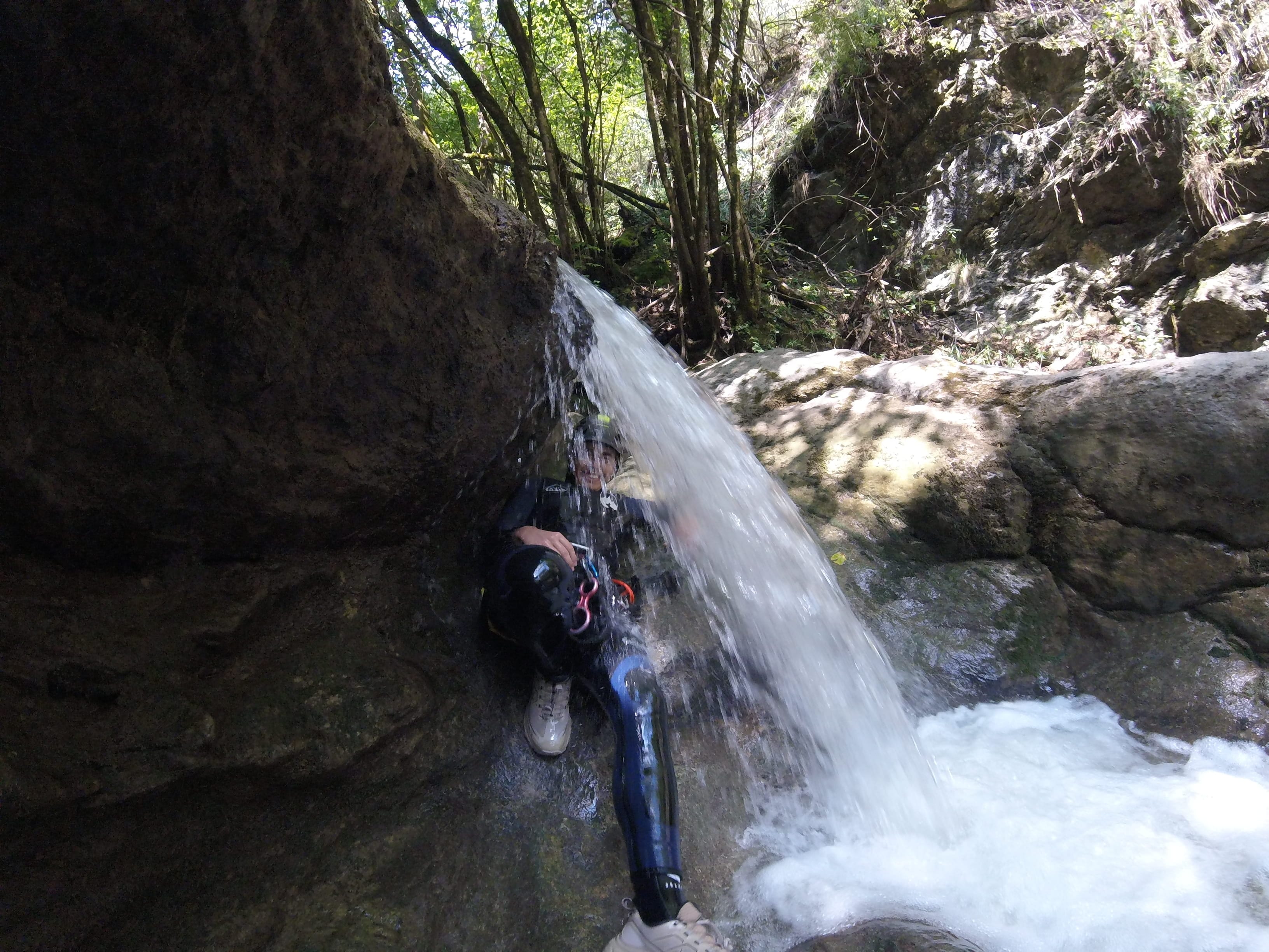 Participant de barranquisme passant sota una petita cascada entre les roques del Barranc del Pamano