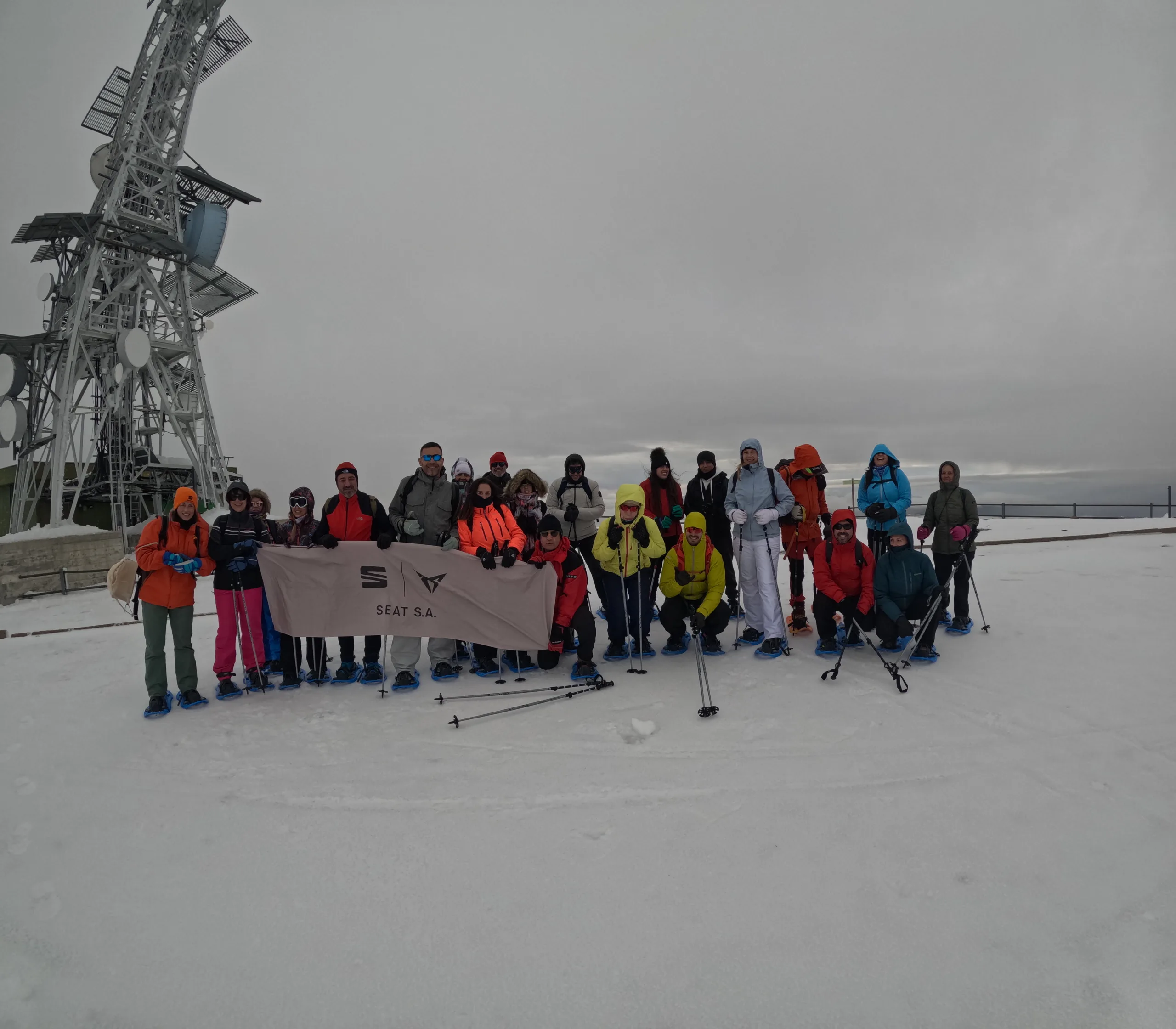 Mejores rutas con raquetas en los Pirineos: grupo de excursionistas con raquetas de nieve posa en la cima junto a una torre de comunicaciones.