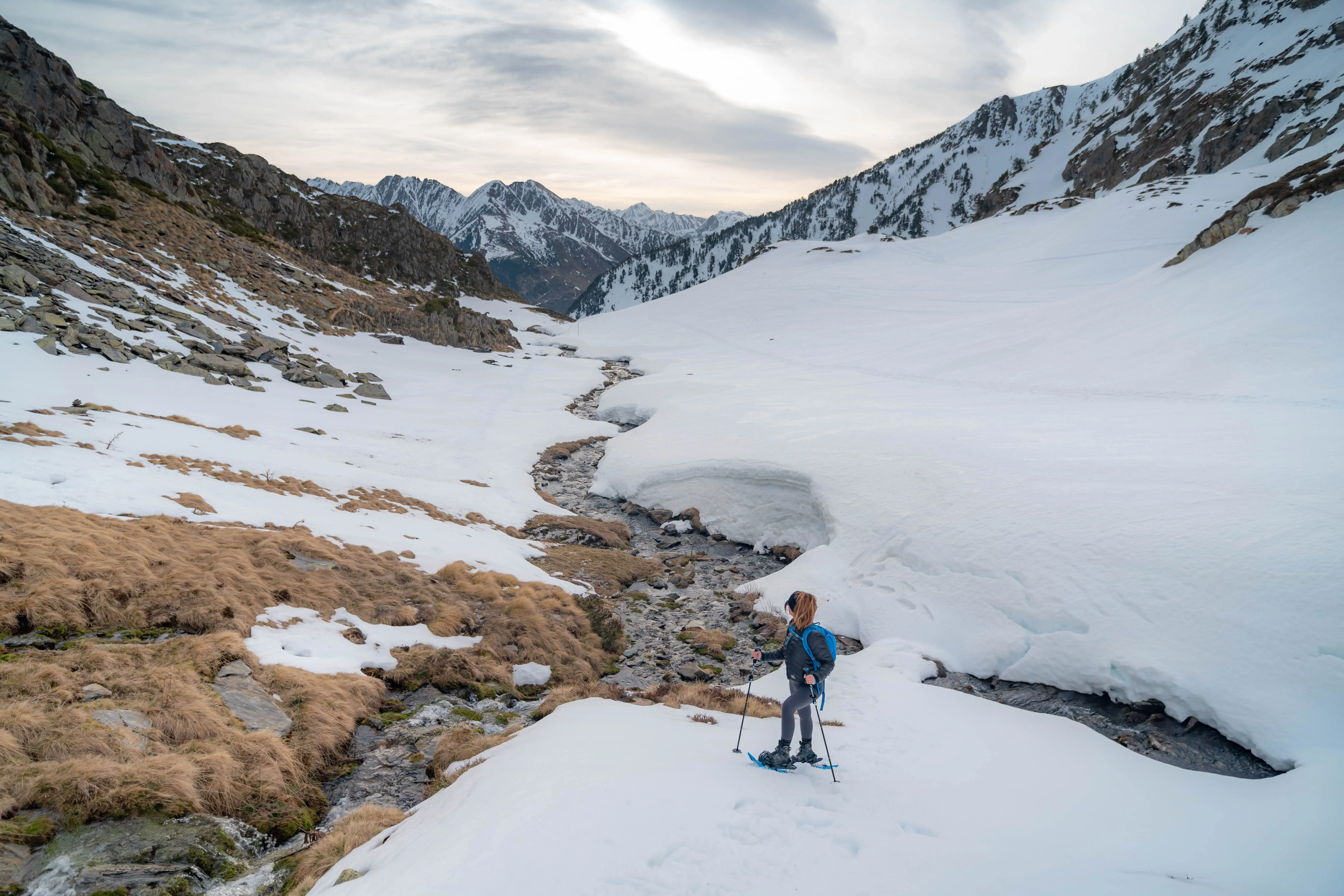 Excursionista con raquetas junto a un arroyo de montaña en el valle nevado bajo el Pic de la Coma del Forn