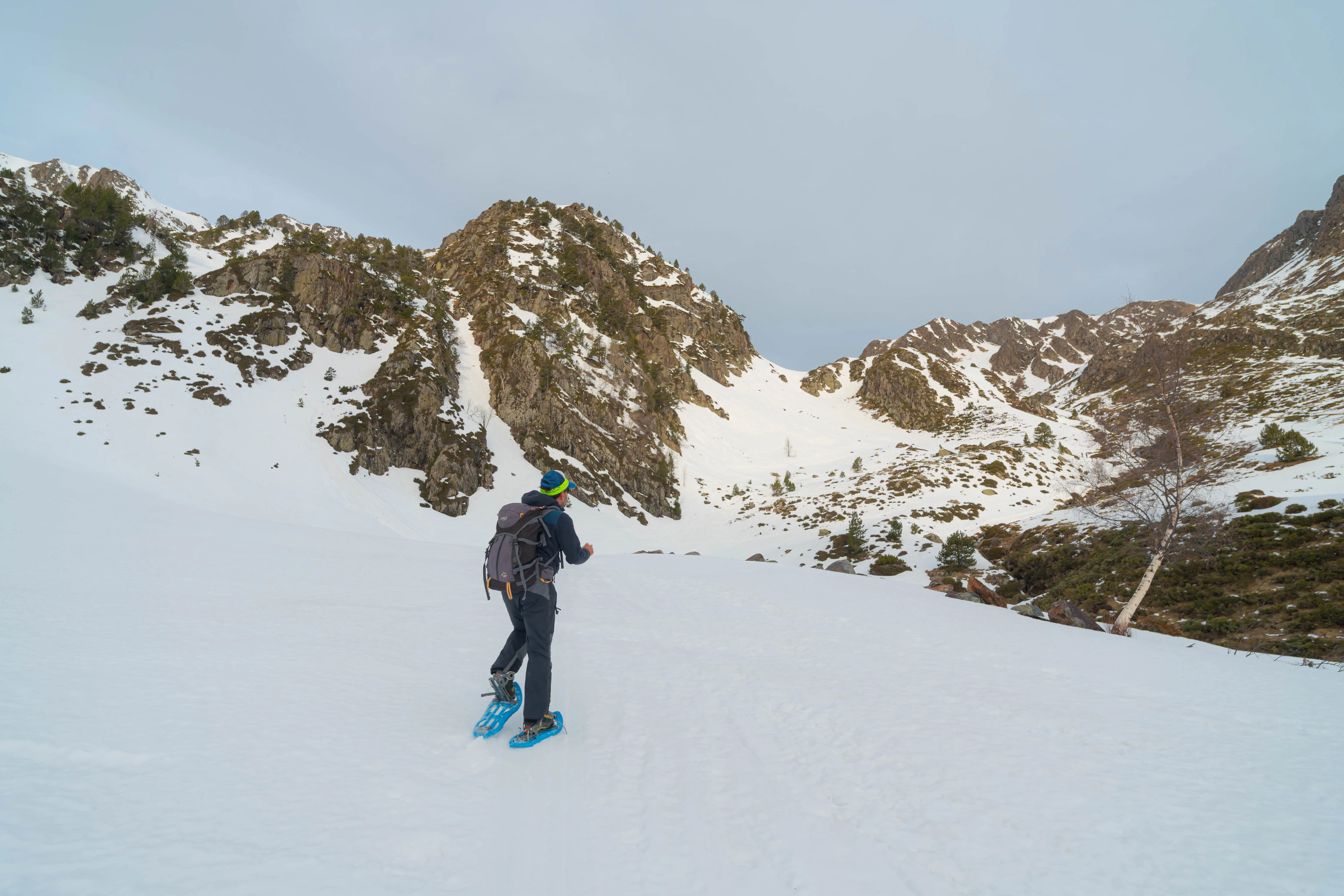 Excursionista con raquetas atravesando una amplia extensión de nieve rodeada de alta montaña durante la ruta al Pic de la Coma del Forn