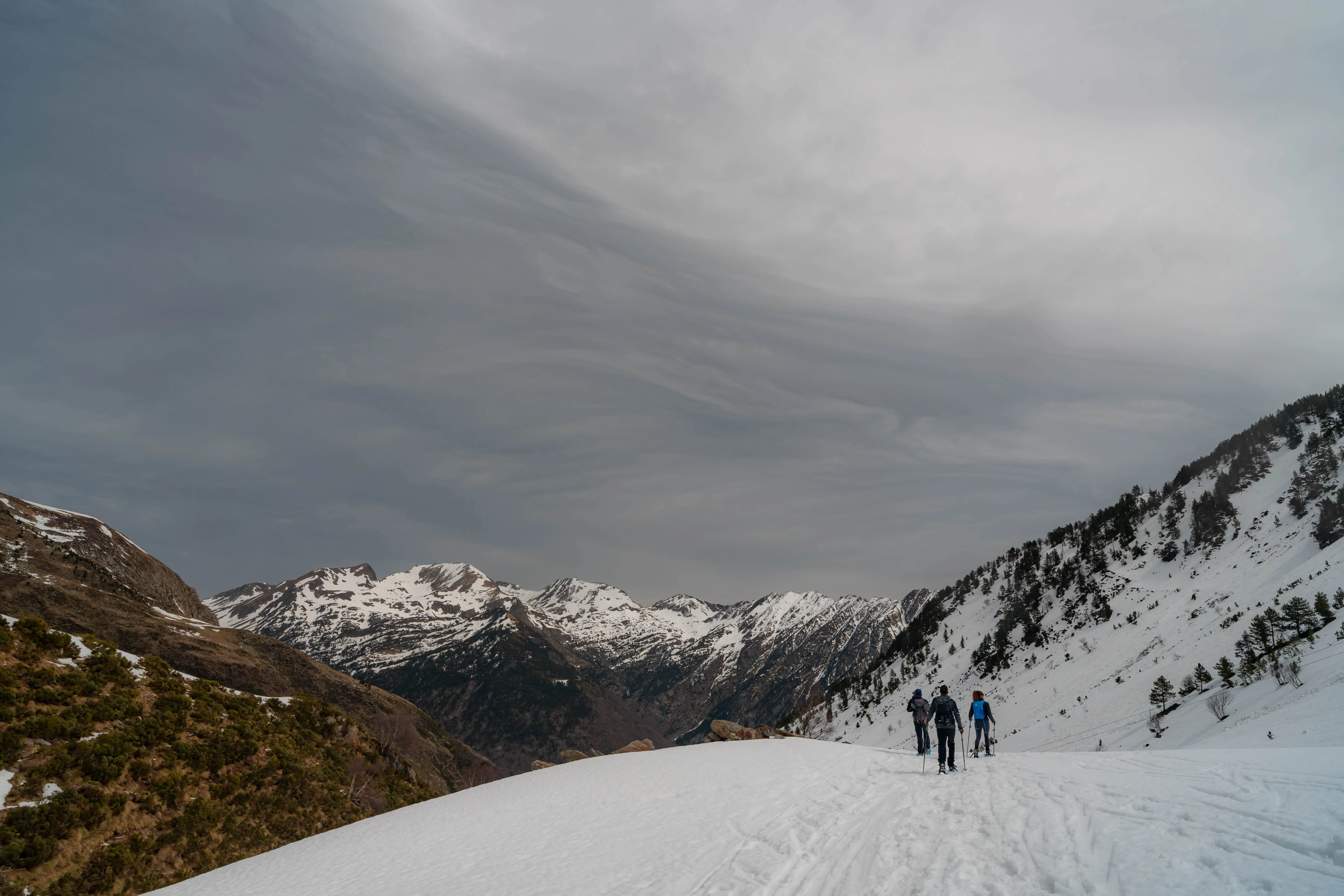 Excursionistas con raquetas descendiendo por un valle nevado rodeado de montañas de los Pirineos cerca del Pic de la Coma del Forn