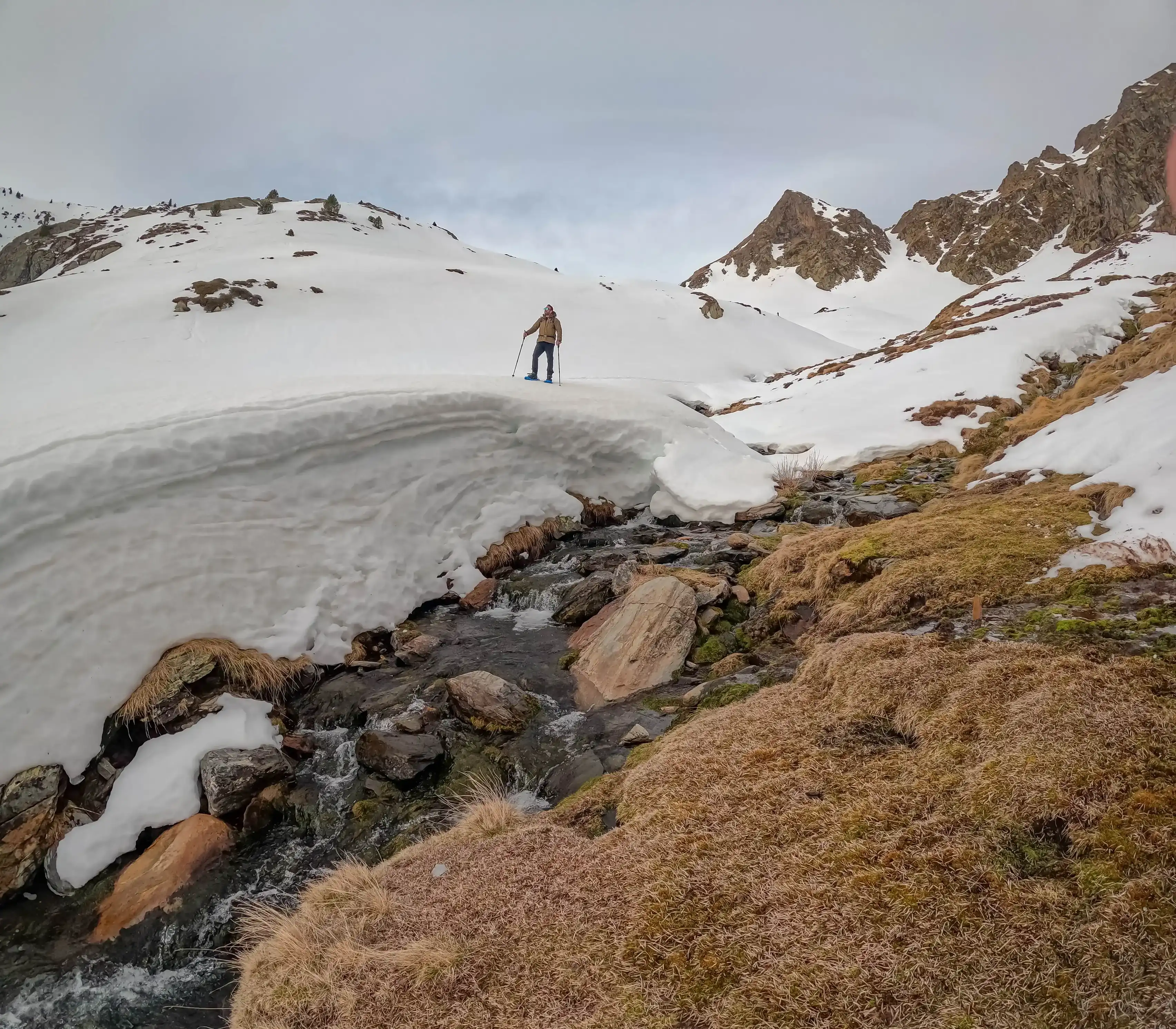 Excursionista con raquetas junto a un arroyo de montaña parcialmente helado durante la ruta al Pic de la Coma del Forn