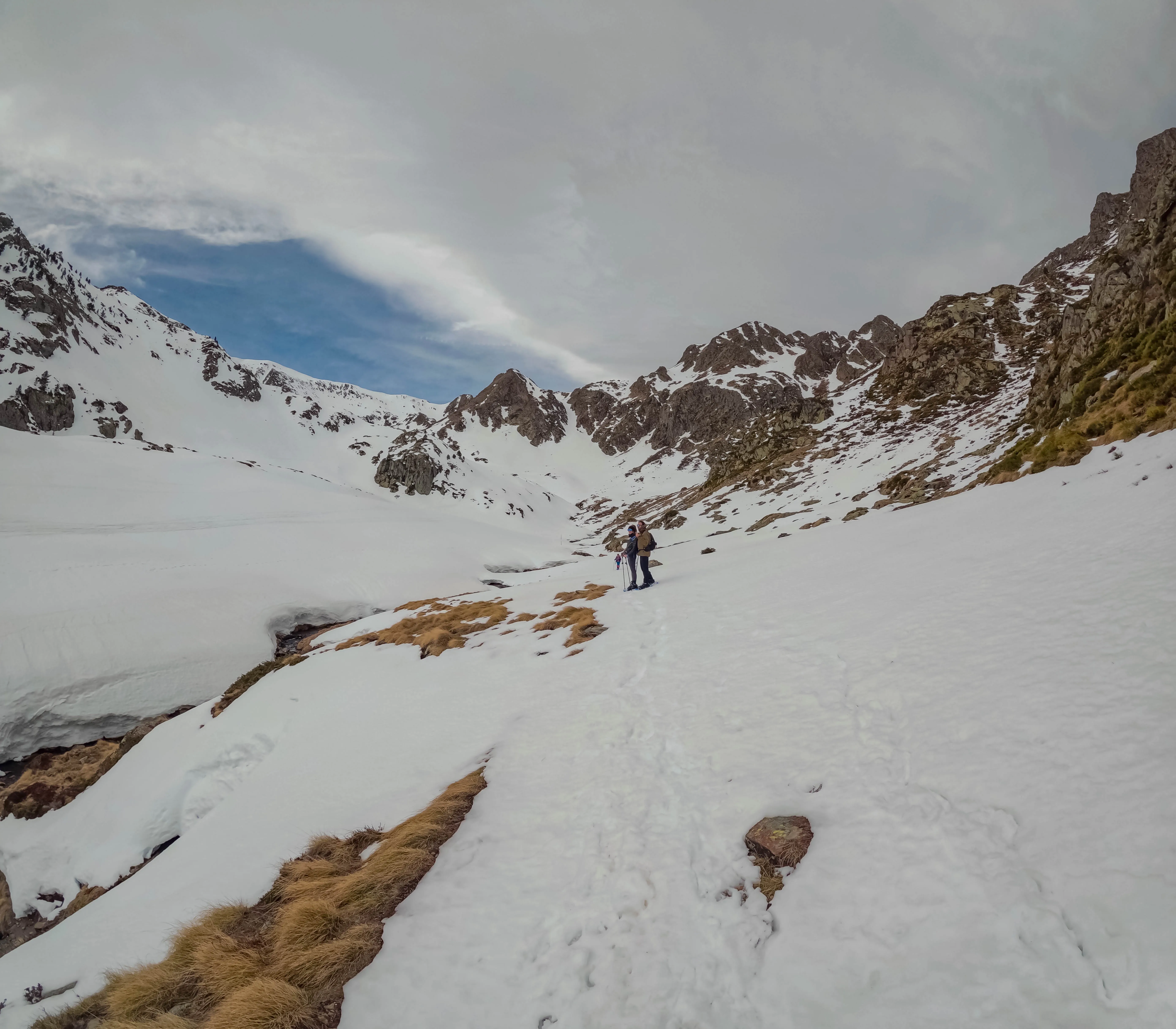 Excursionista con raquetas atravesando un valle de montaña nevado rodeado de cumbres rocosas durante la ruta al Pic de la Coma del Forn