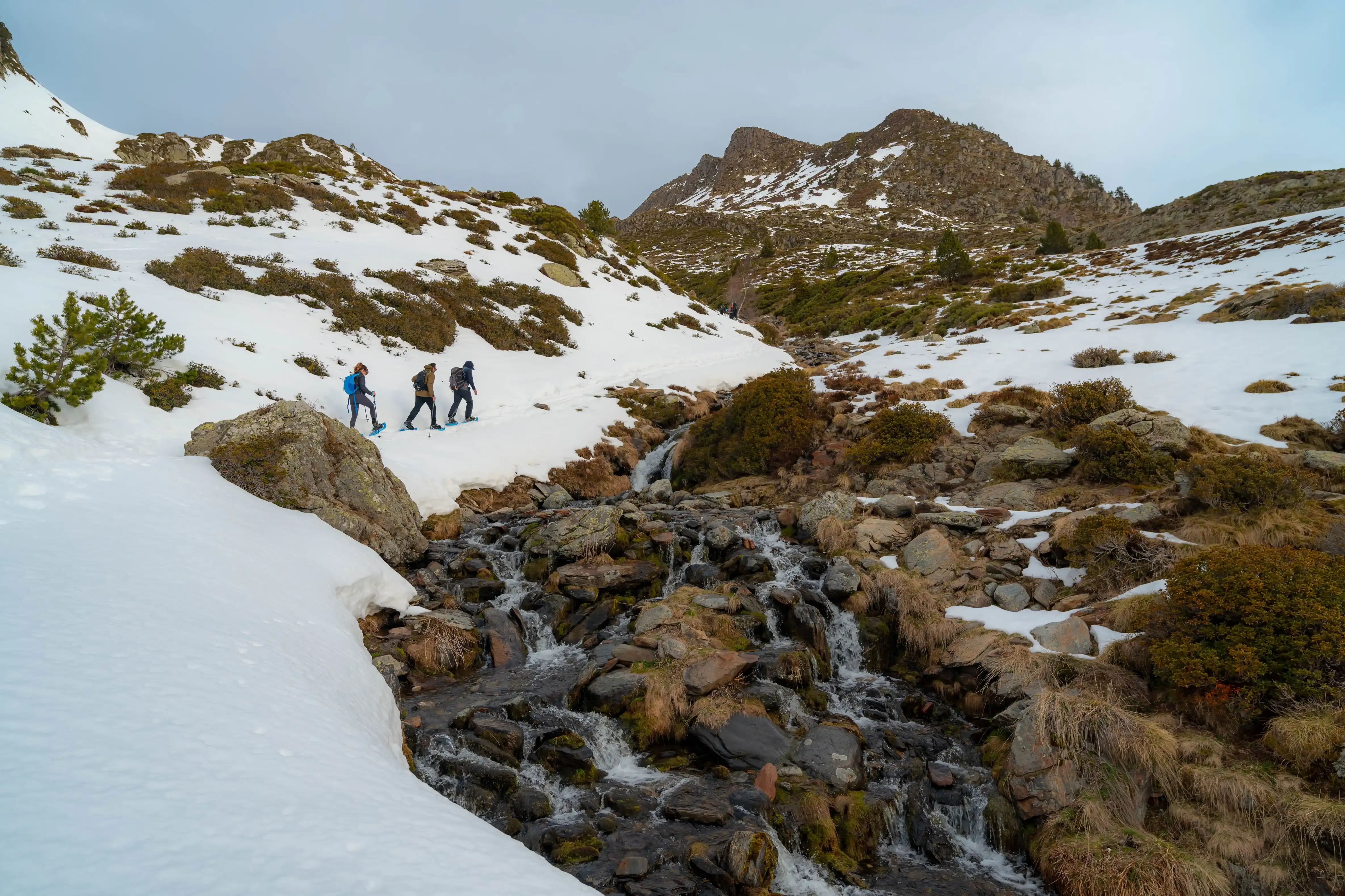 Excursionistas con raquetas siguiendo un arroyo de montaña en un paisaje nevado durante la ruta al Pic de la Coma del Forn
