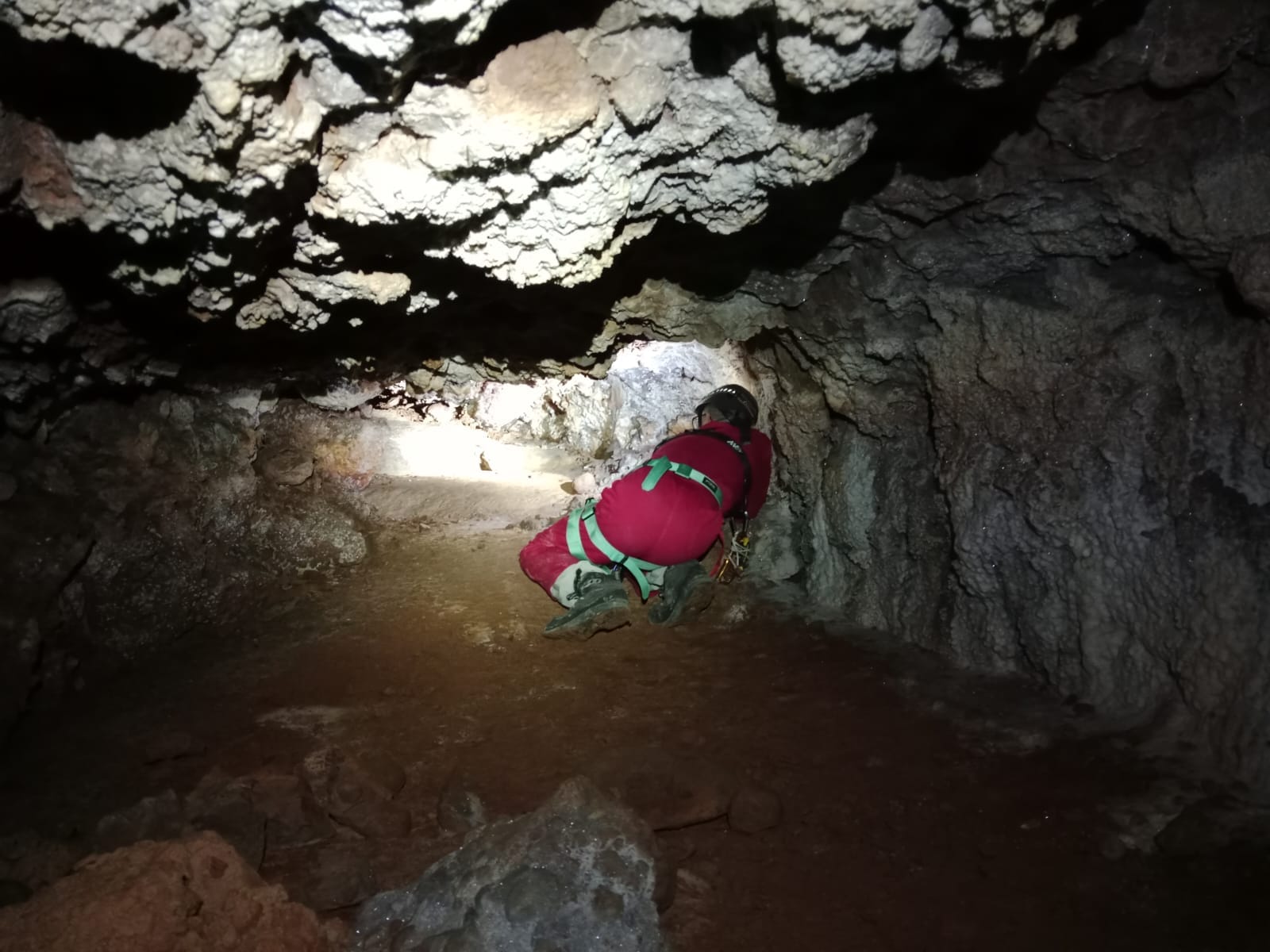 Espeleòleg avançant per un pas baix i estret entre les roques a l’interior de la Sima del Barbuxell