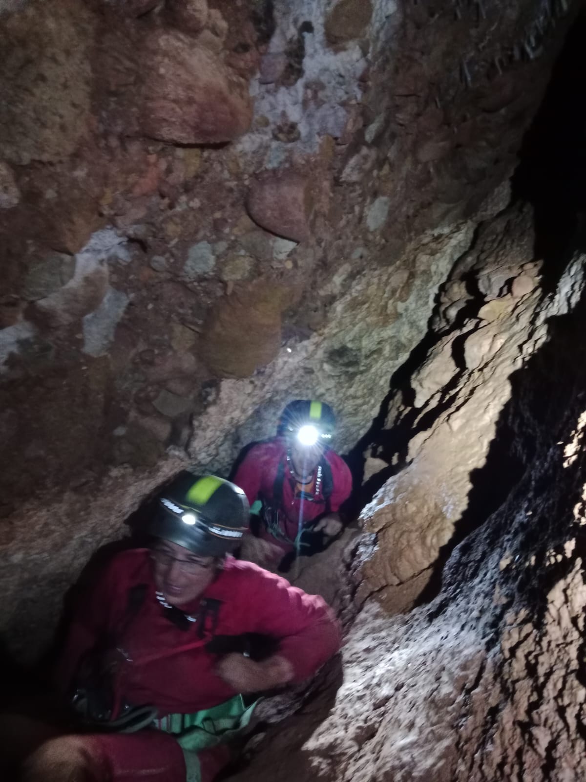 Espeleòlegs amb casc i llum frontal avançant per un pas estret i rocós a l’interior de la Sima del Barbuxell