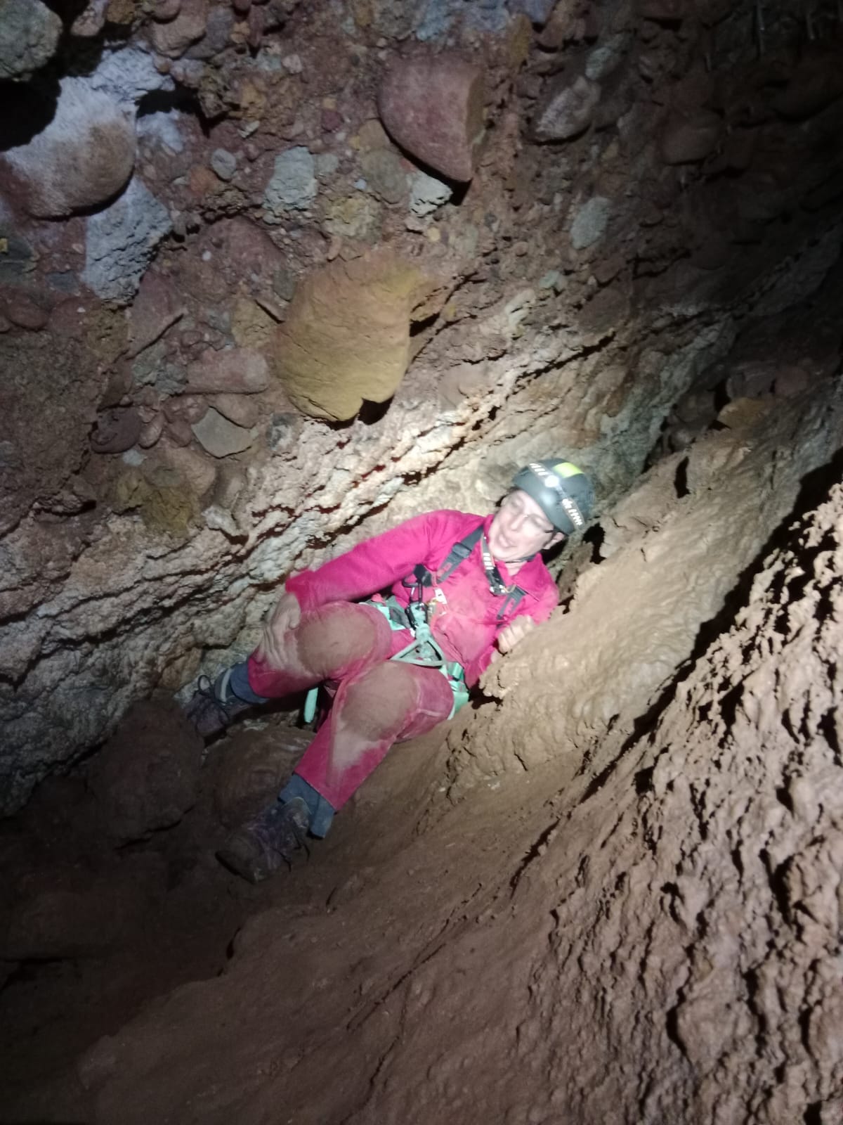 Espeleòleg amb casc i equip tècnic avançant per un pas estret i inclinat a l’interior de la Sima del Barbuxell